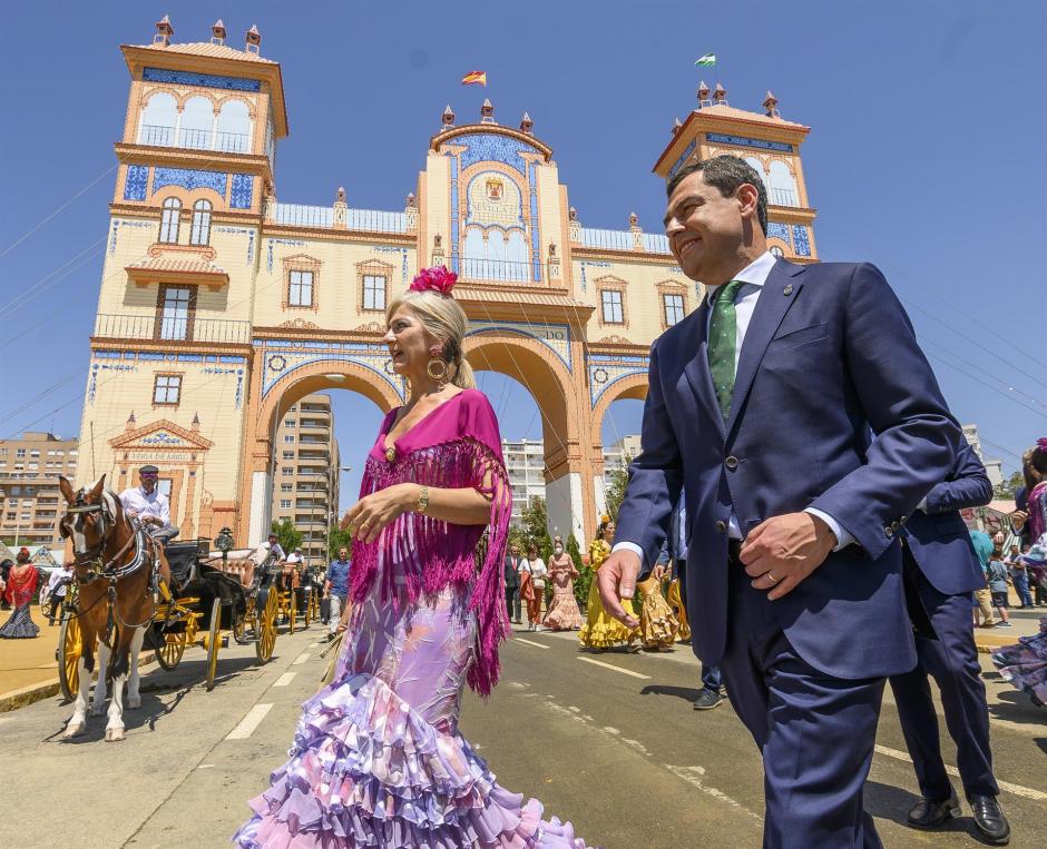 El presidente de la Junta de Andalucía, Juanma Moreno y la consejera de Cultura, Patricia del Pozo, pasan junto a la portada de la Feria de Abril de Sevilla