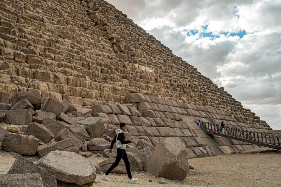 Un visitante camina junto a las piedras de la base de la Pirámide de Micerino