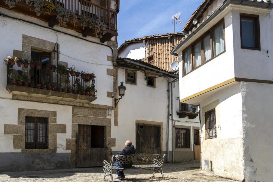 Turista sentado en un banco contemplando los balcones llenos de macetas en Candelario