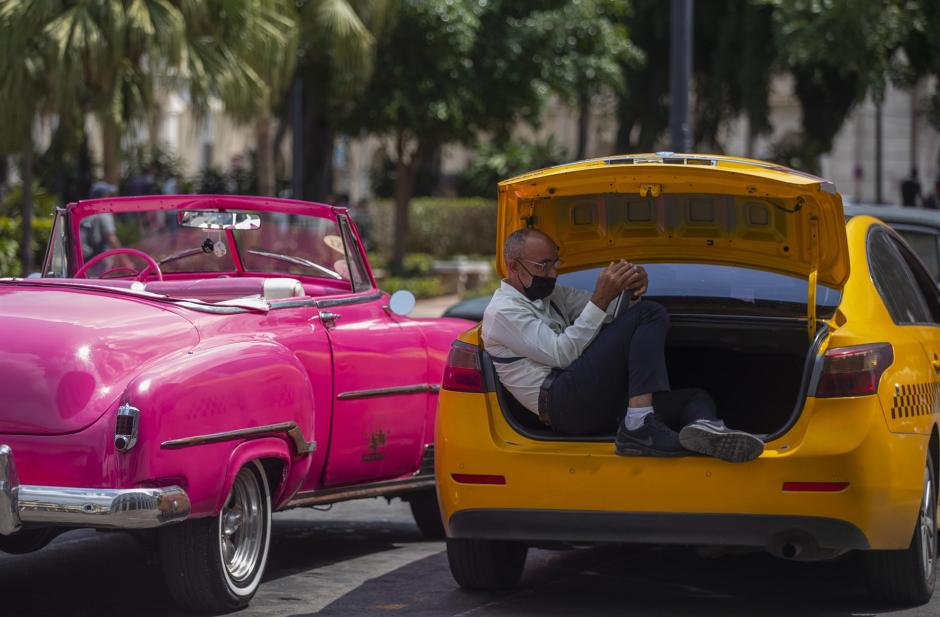 Un taxista se protege de sol sentado en el maletero del coche, mientras espera clientes hoy en La Habana