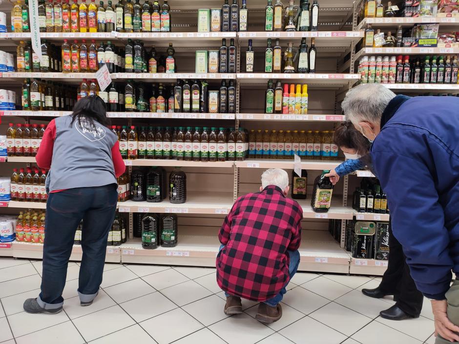 Varias personas compran aceite en un supermercado de Madrid, donde algunas estanterías permanecen vacías