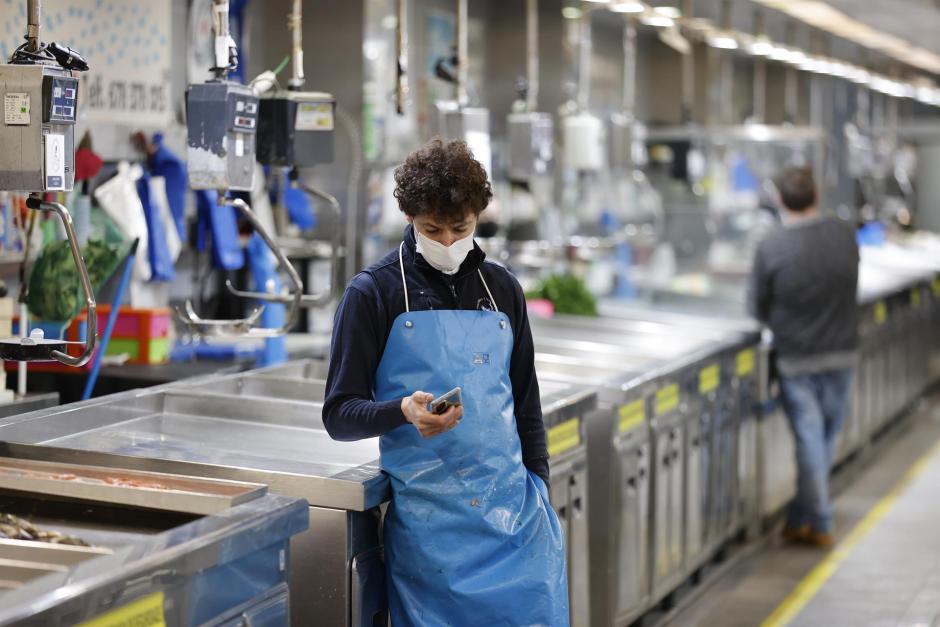 Uno de los pescaderos del mercado coruñés de la Plaza de Lugo revisa su teléfono móvil al lado de unos mostradores vacíos, el jueves