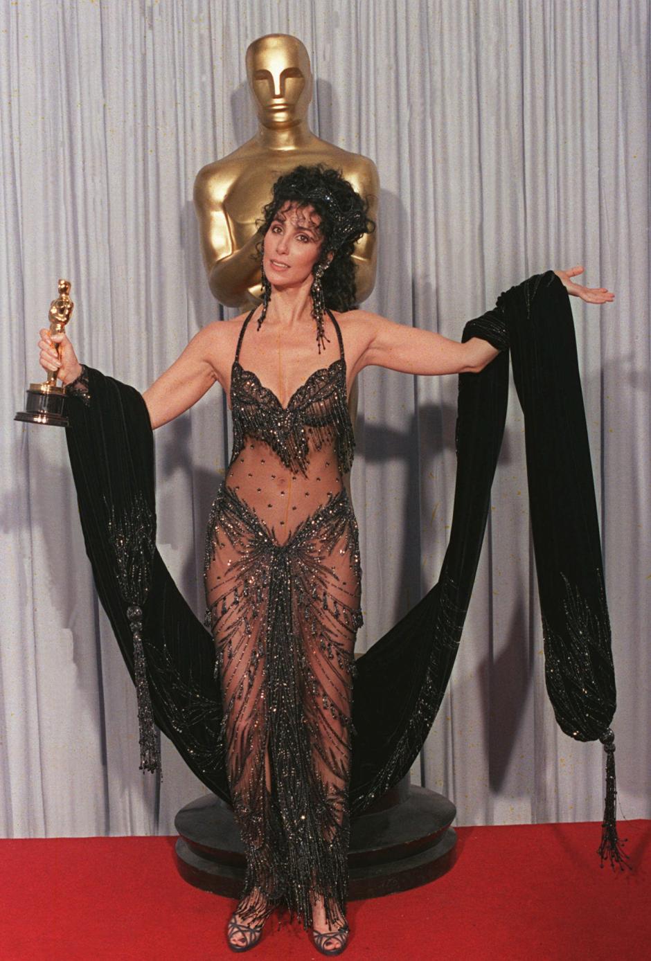 FOR USE WITH FEATURE PACKAGE FOR FRIDAY, MARCH 21--FILE--Cher shows off her Oscar for best actress and her Bob Mackie black sequined see-through gown after winning the award for her role in "Moonstruck" at the Academy Awards April 12, 1988, in Los Angeles. Cher is among the famous and not-so-famous who have used the Oscars ceremony as a forum for both private and political messages. (AP Photo/Files)© RADIAL PRESS