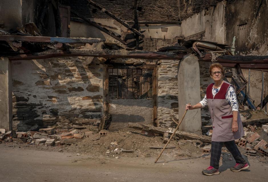 Una vecina pasea junto a una vivienda calcinada tras el incendio forestal de El Barco de Valdeorras