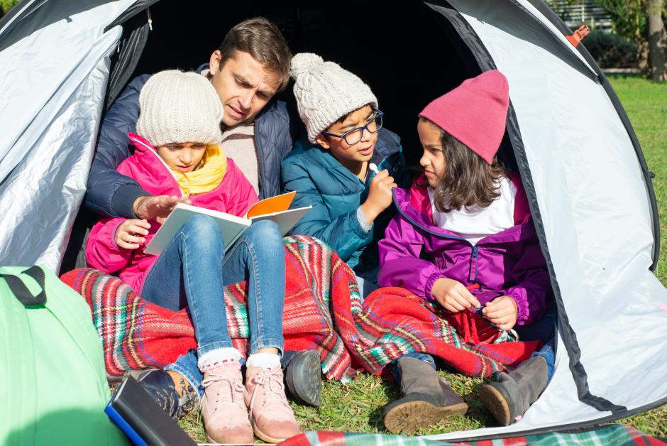 Niños leyendo con sus padres en un camping