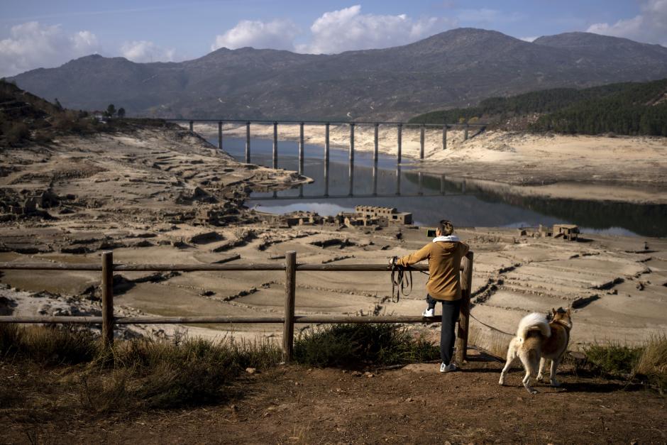 A man photographs the old village of Aceredo, submerged three decades ago when a hydropower dam flooded the valley and emerged now due to drought at the Lindoso reservoir, in northwestern Spain, Saturday, Feb. 12, 2022.