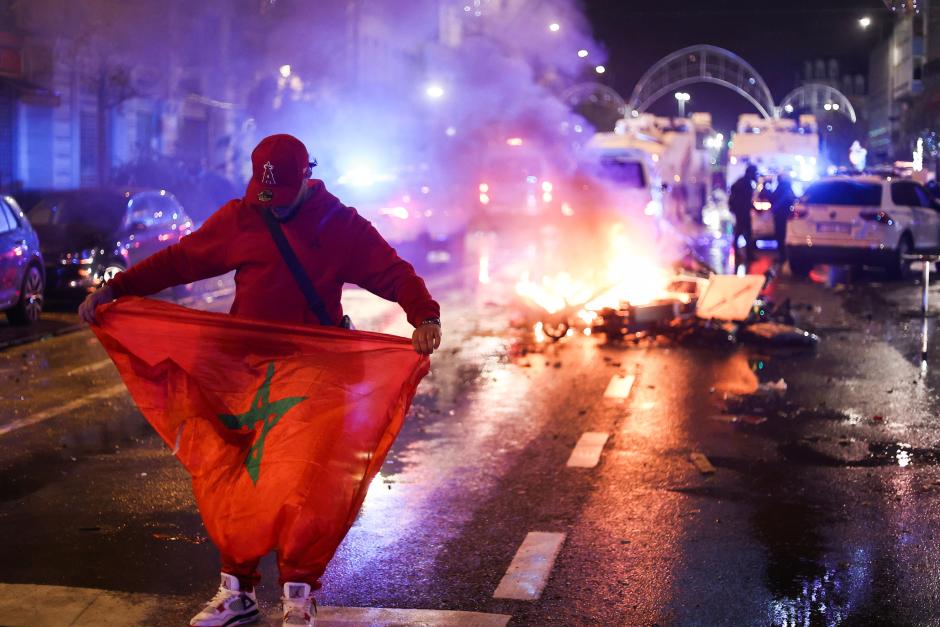 Un fanático sostiene una bandera marroquí mientras los scooters eléctricos se queman en la espalda en Bruselas