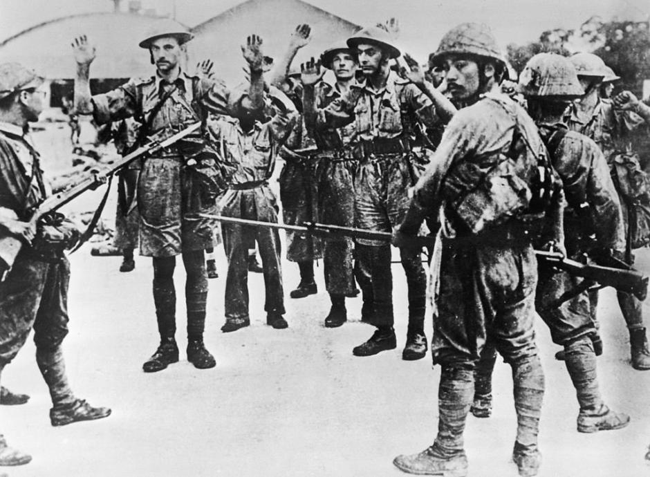 Las tropas del Regimiento de Suffolk que se rinden son retenidas a punta de pistola por la infantería japonesa