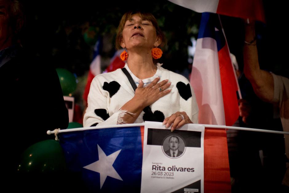 A woman holds a Chilean national flag and an image of slain police officer Rita Olivares during a vigil in memory of murdered officers, in front of the Carabineros de Chile building in Santiago on March 27, 2023. - Armed crime, hit men, extortion and human trafficking are the main concern of Chileans, according to surveys, and they have pressured the Government and Congress to deal with a battery of laws against crime, including one considered by international organizations of "easy trigger" for police officers. (Photo by Pablo VERA / AFP)