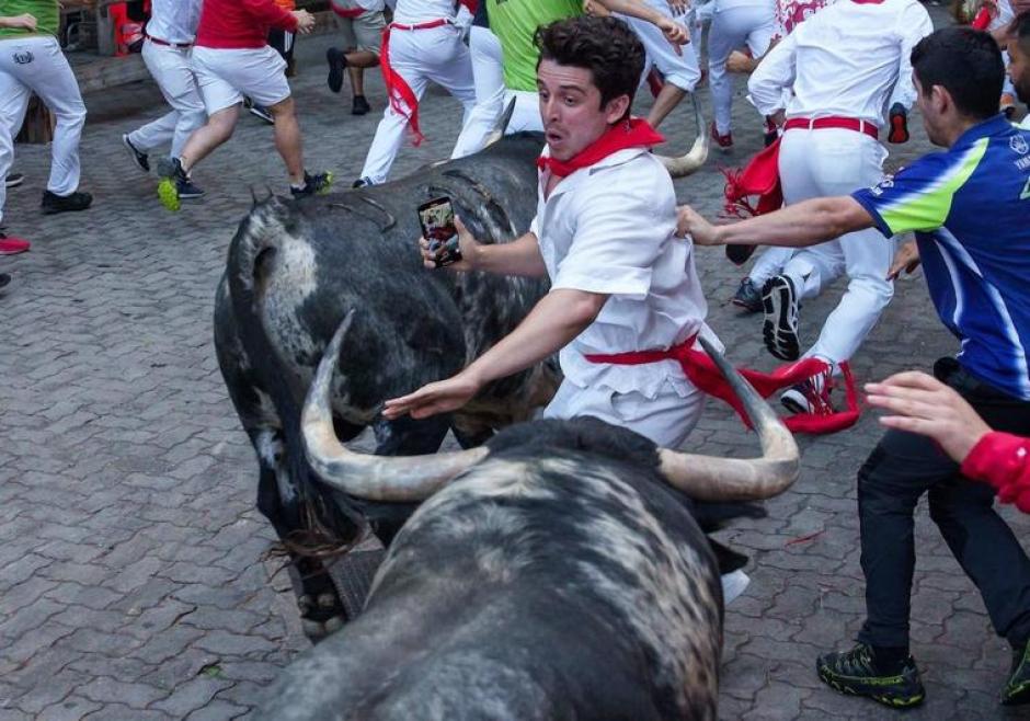 Un corredor se zafa entre dos toros con la cámara del móvil encendida en el encierro de este domingo en San Fermín