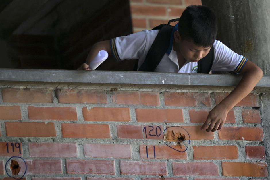 A schoolboy at the Jose Maria Obando school, points at some of the holes of the shots left by the combats that took place on September 5 between the Colombian Police and the FARC EP dissidence Dagoberto Ramos front, in Corinto, department of Cauca, on September 13, 2023. (Photo by JOAQUIN SARMIENTO / AFP)