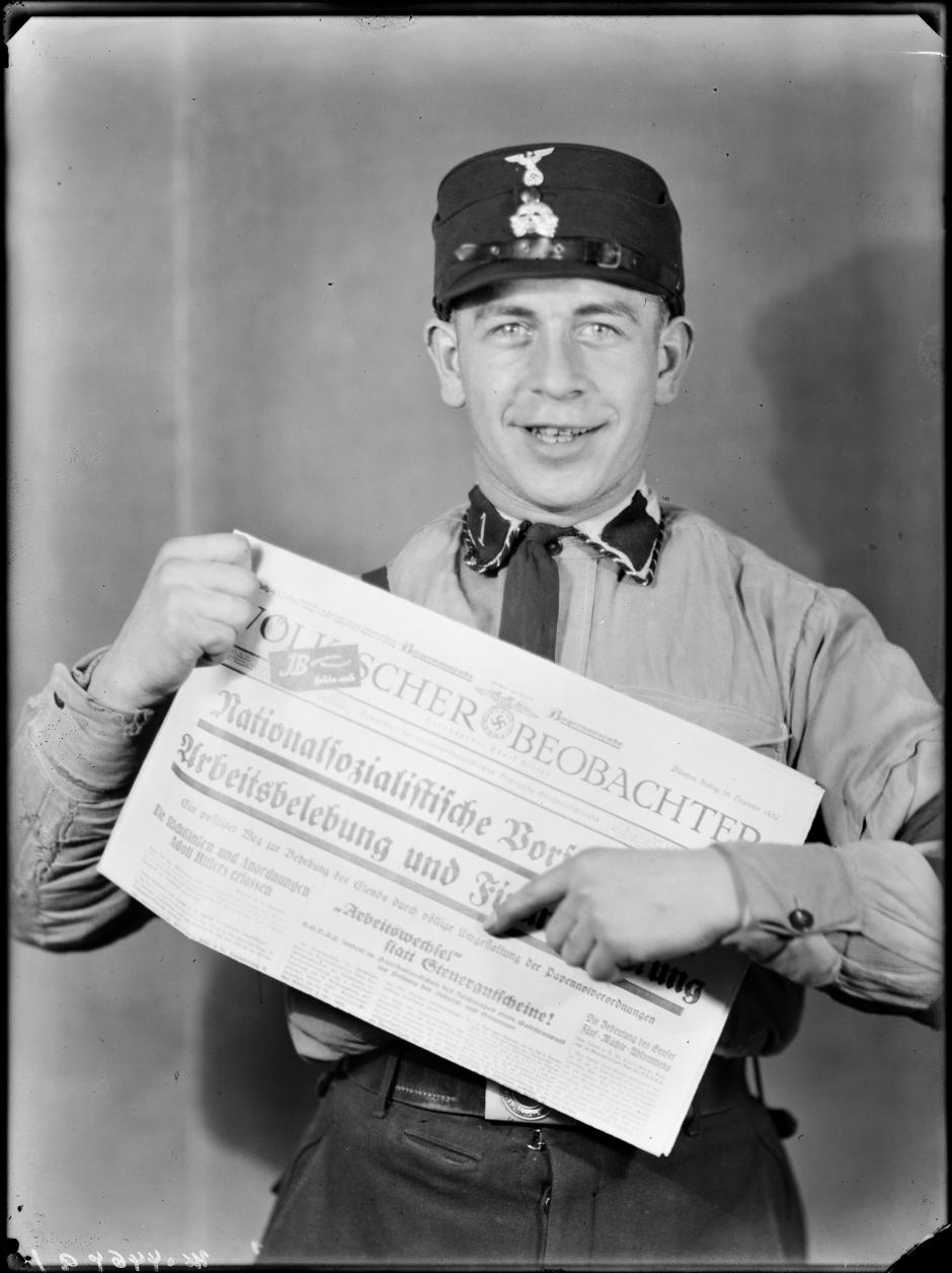 Foto promocional de un miembro uniformado de las SS con un número de 1932 del órgano del Partido Nazi Völkischer Beobachter, en el que se señala "Antes cambio de trabajo que créditos fiscales"