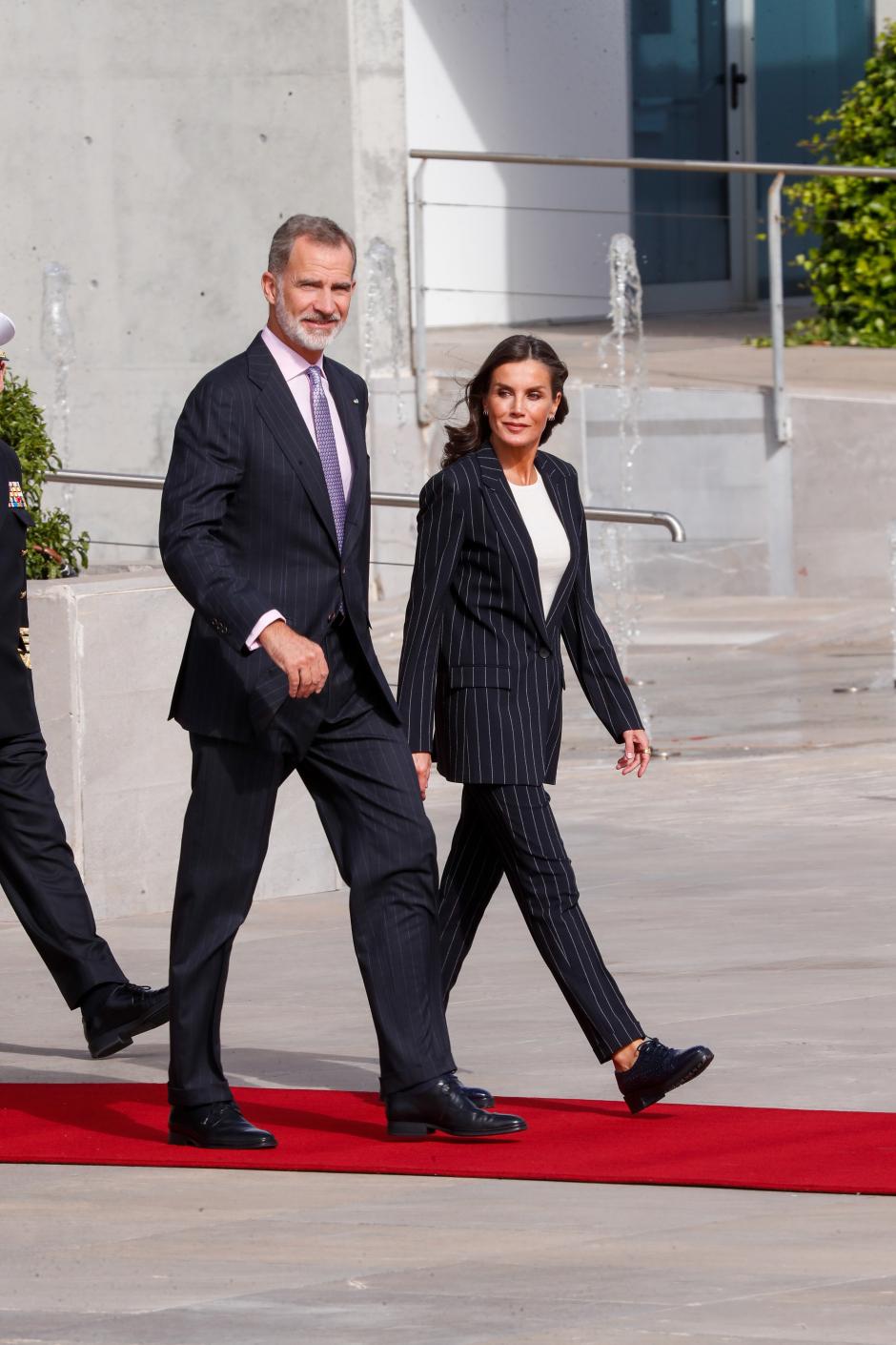 En su visita de Estado a Alemania optaba por un look sobrio y clásico a la par que cómodo para viajar compuesto por un traje de chaqueta de raya diplomática. El toque casual lo daba la camiseta básica blanca. Sin embargo, lo que más llamaron su atención fueron sus pies puesto que lucía unos viejos mocasines azul marino de Uterqüe con suela de goma. La Reina prefería ir cómoda, prescindiendo de tacones debido al neuroma de Morton que tiene en su pie izquierdo, además de la metatarsalgia crónica que sufre desde hace años.