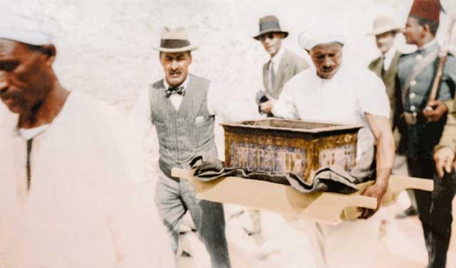 Howard Carter acompaña a la figura de madera con el retrato de Tutankamón (el llamado maniquí, Carter nº 116, de finalidad incierta) de camino al taller (tumba KV 15, de Sethos II). Sentado en la pared de la izquierda está Lord Carnarvon; detrás de él camina Arthur Weigall, antiguo inspector del Servicio de Antigüedades