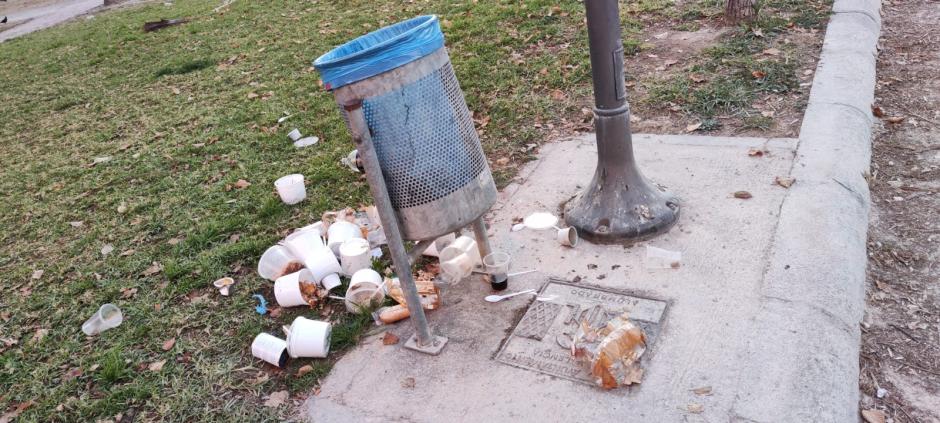 Varios recipientes de comida se amontonan fuera de una papelera del parque del Turia