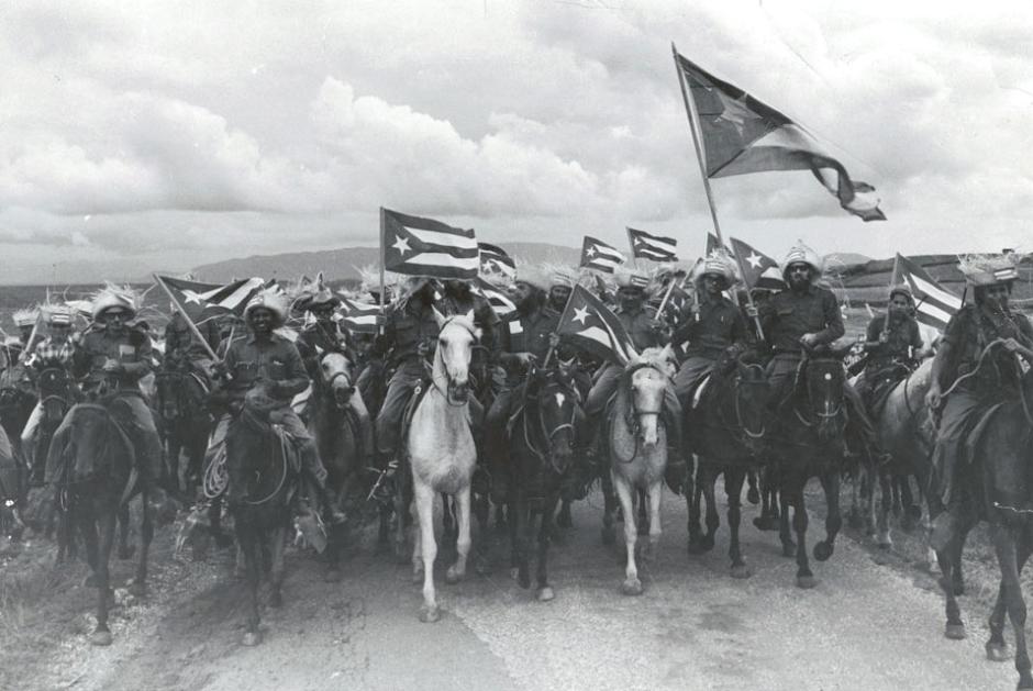 La imagen muestra a un grupo de rebeldes del Movimiento 26 de Julio de Fidel Castro montados a caballo y blandiendo banderas cubanas azotadas por el viento