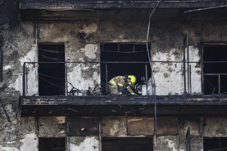 Bomberos y Policía Científica inspeccionan un cuerpo en un balcón del edificio incendiado en el barrio de Campanar de Valencia