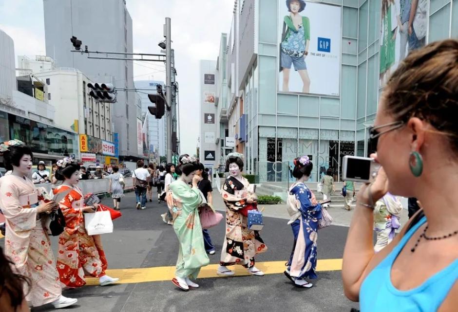 Una turista fotografía a un grupo de geishas que pasean por el distrito de Omotesando, en Tokio
