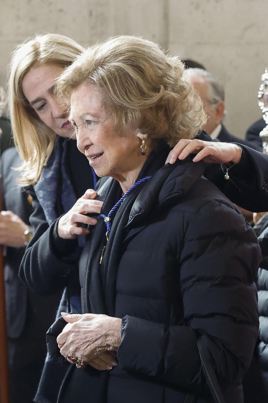 La Infanta Cristina ayuda a su madre, Doña Sofía, a colocarse la medalla de honor de la cofradía del Santísimo Cristo de los Alabarderos