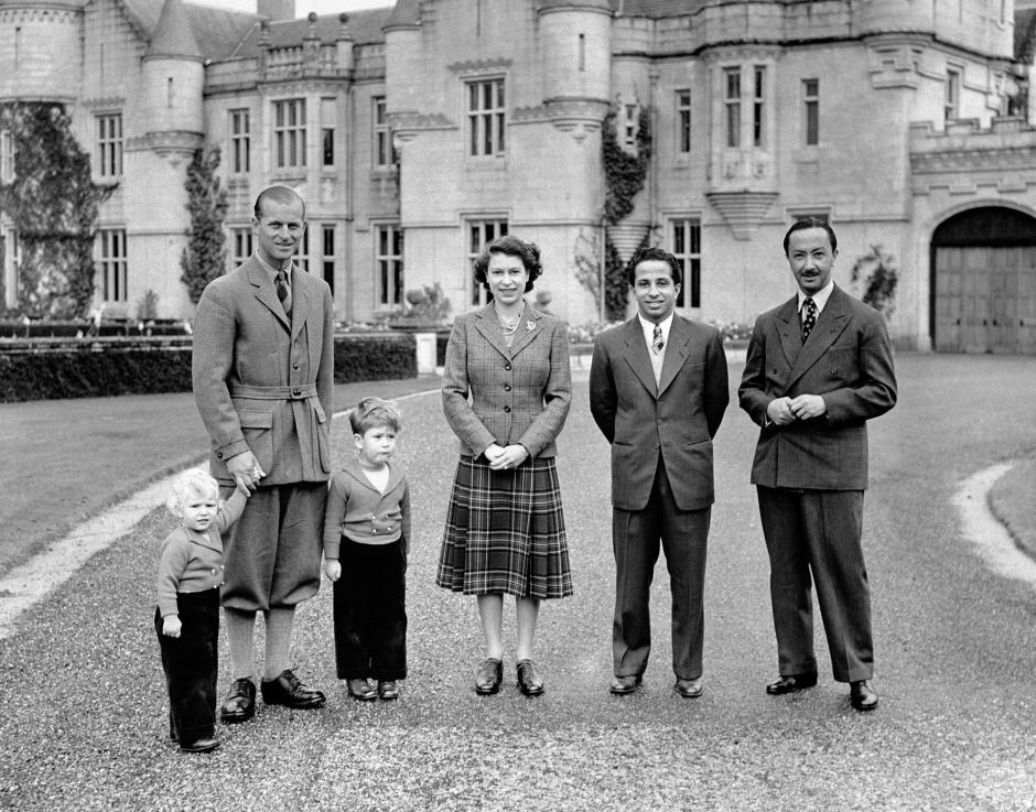 Queen Elizabeth II, wearing a tartan skirt and tweed jacket outside Balmoral Castle with her Royal visitors, King Faisal II and the Regent of Iraq, and the Duke of Edinburgh, Prince Charles and Princess Anne.