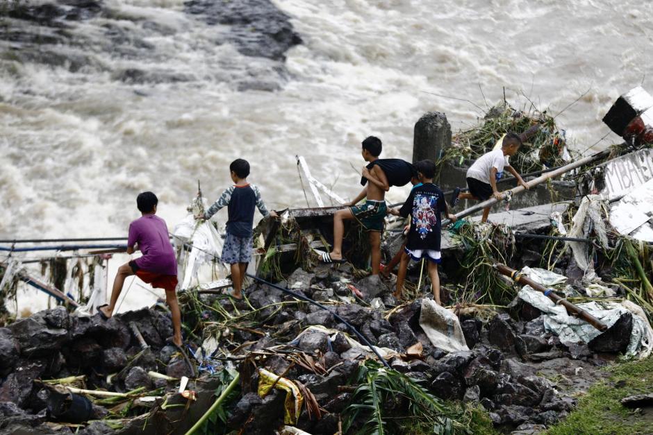 Unos niños observan un dique de control de inundaciones dañado Filipinas