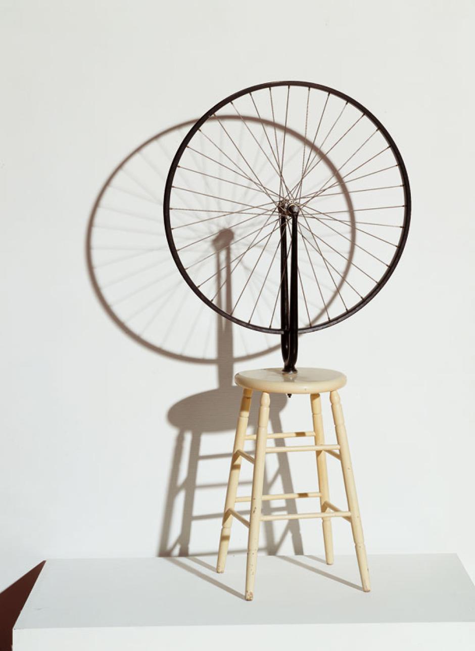 Otra obra que todo el mundo identifica con Duchamp es la Rueda de Bicicleta. Al igual que pasó con La Fuente, la original se perdió y la actual fue reproducida también por la Galería Schwarz en 1964. Consiste en una rueda de bicicleta atornillada a un taburete y puesta del revés. Es uno de los ejemplos más claros de ready-made, donde un objeto cotidiano se convierte en obra de arte solo porque así lo ha querido el artista.