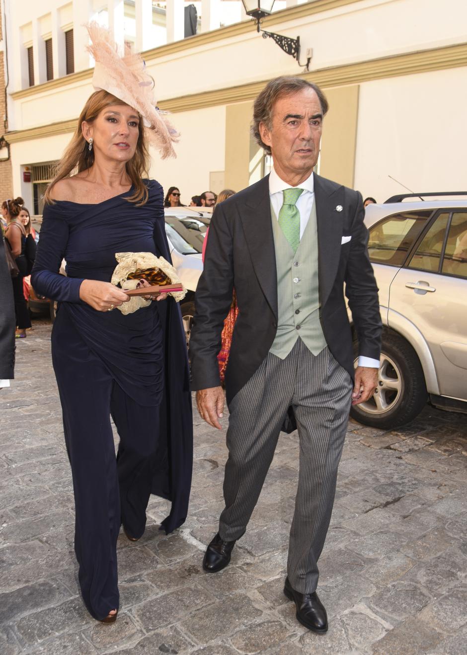 La madre de la novia, con un mono en azul medianoche con capa, detalles drapeados y cinturón con hebilla. Lo ha combinado con tocado de plumas, clutch carey y zapatos de tacón con plataforma.