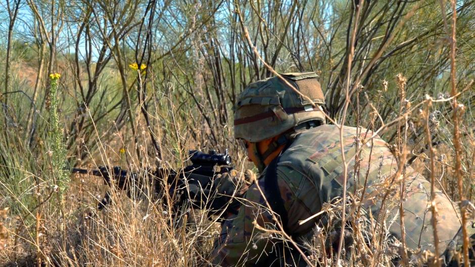 Un soldado armado agazapado en la maleza defiende su posición ante el fuego enemigo