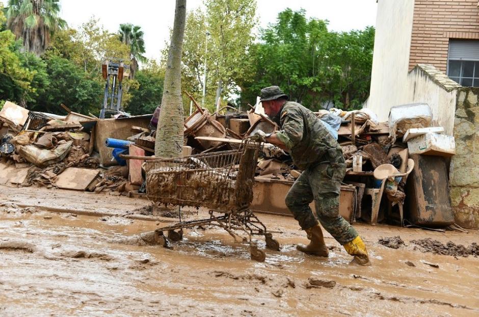 Un militar lleva un carro de supermercado lleno de residuos generados por la DANA