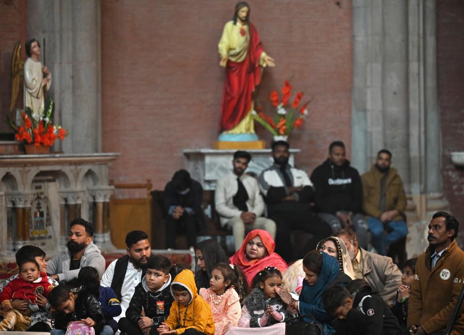 Una pareja musulmana junto a la hoguera ante el santuario de la Virgen María durante el servicio de Nochebuena en la catedral católica siríaca del Sagrado Corazón en la ciudad meridional iraquí de Basora el 24 de diciembre de 2024