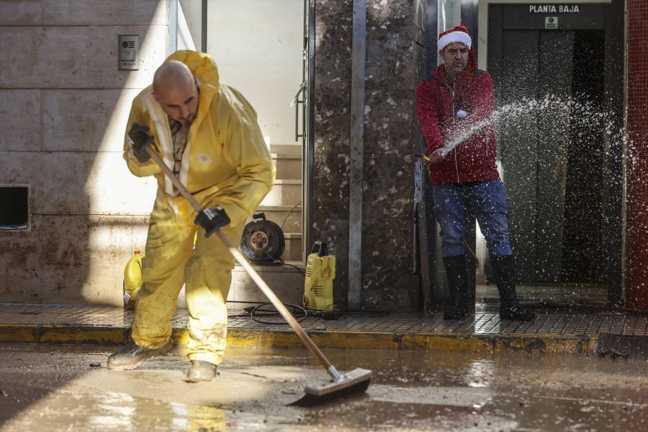 Un hombre con un gorro de Papá Noel ayuda a limpiar una calle de Paiporta