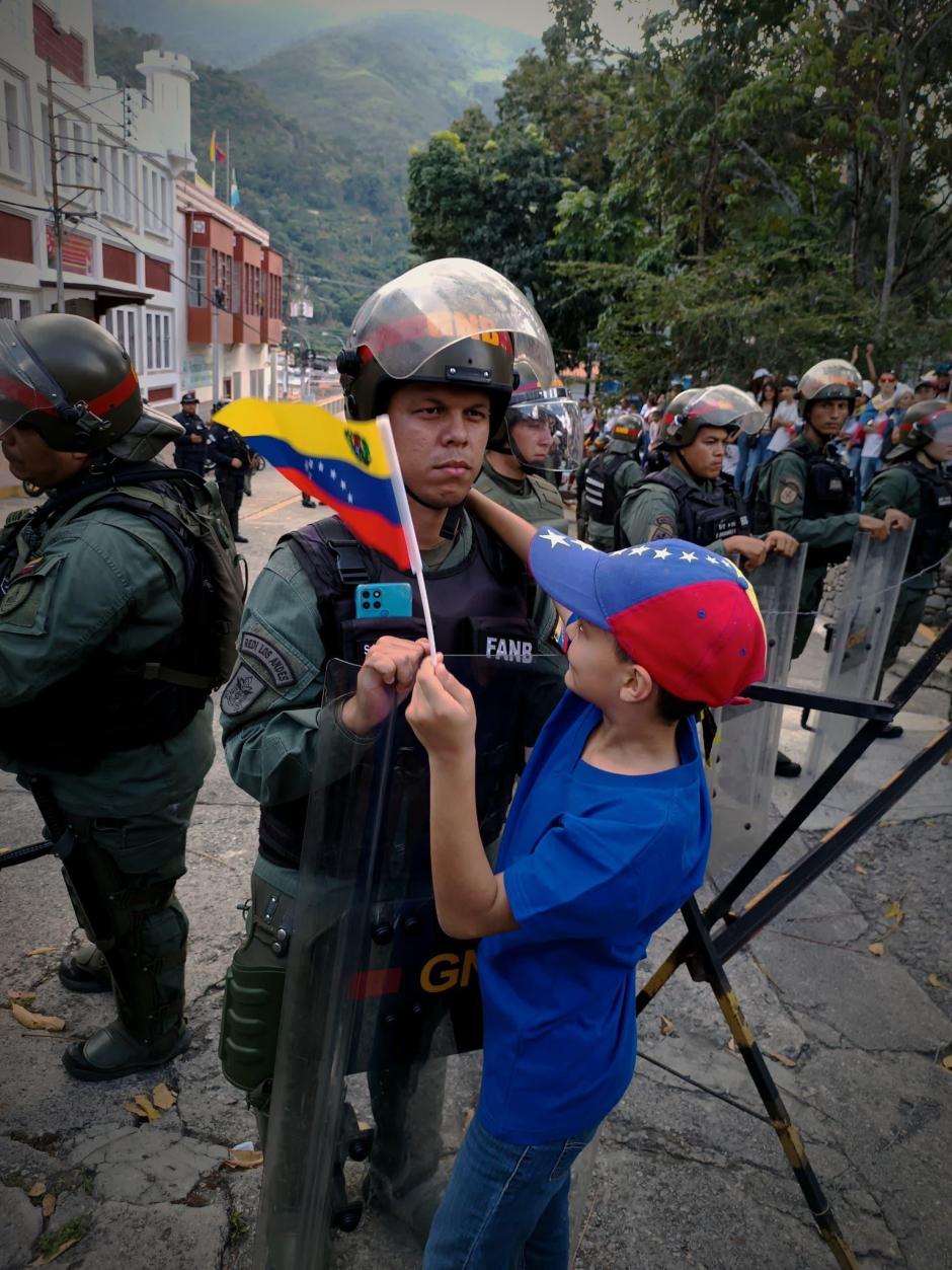 Un niño se acerca a un militar con la bandera de Venezuela