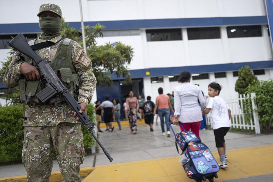 Un niño entra al colegio mientras un militar vigila el centro