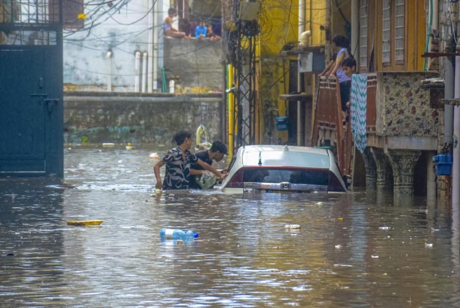 Boys look at a submerged vehicle in a water-logged street in Rawalpindi, Pakistan, July 17, 2025. Heavy monsoon rains continue in Pakistan, causing flooding, landslides and urban flooding in several provinces. (Photo by Raja imran / Middle East Images via AFP)