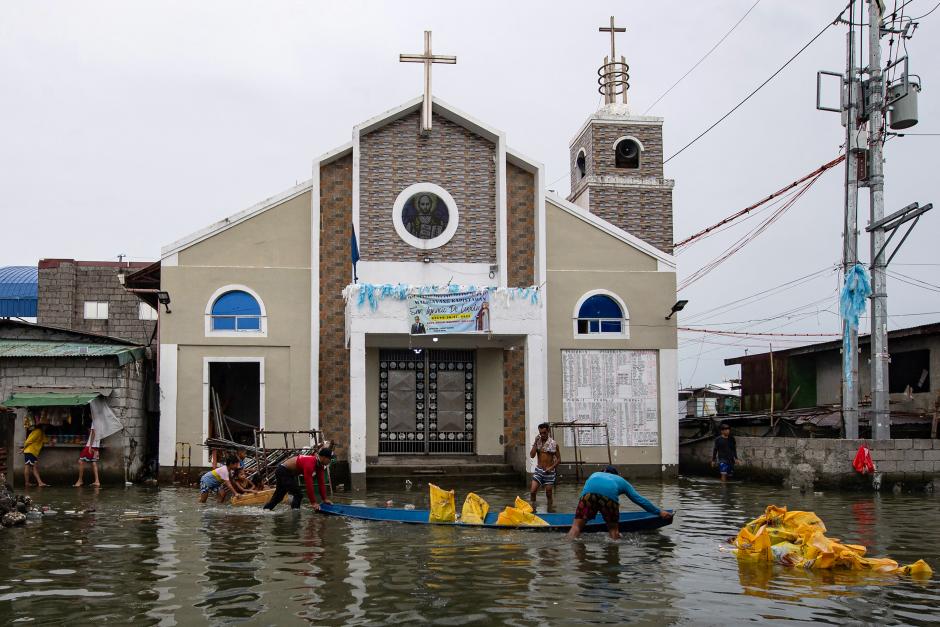Obreros descargando sacos de arena en una obra frente a una iglesia en una calle inundada de Isla Pugad