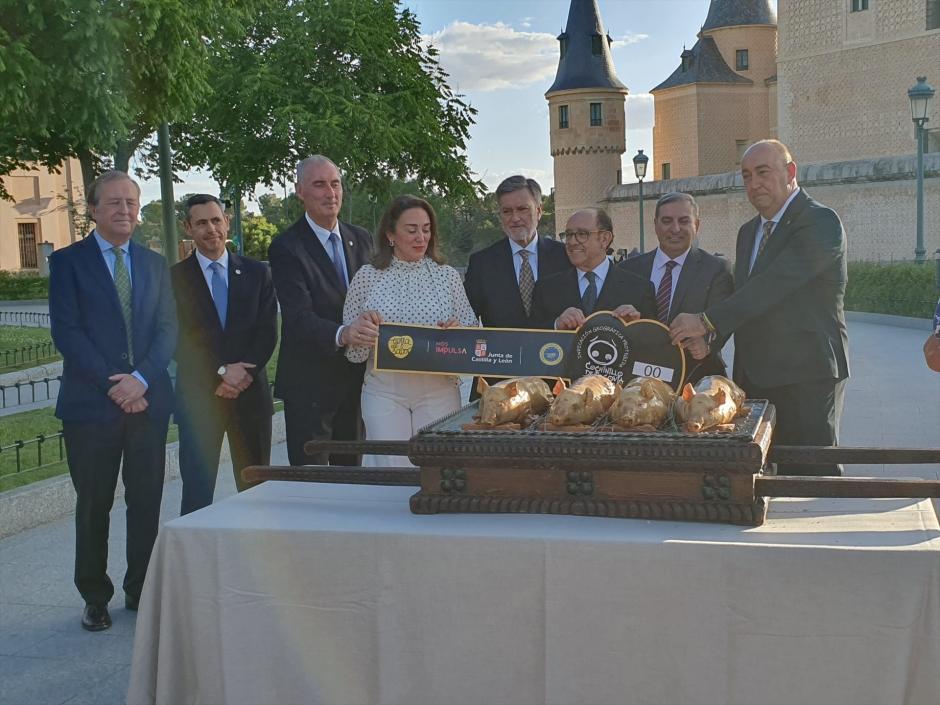 La consejera González Corral y el hostelero José María Ruiz (centro) sujetan una muestra de vitola ante varios cochinillos asados