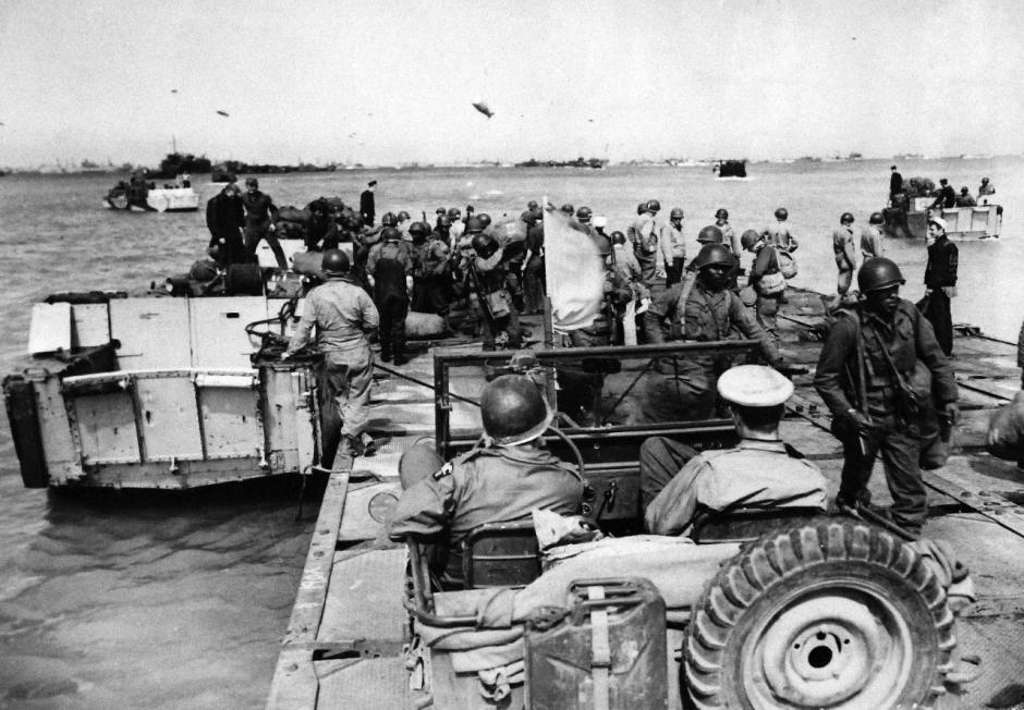 Refuerzos estadounidenses desembarcan en Normandía. Tropas afroamericanas estadounidenses desembarcan de una lancha de desembarco en un muelle provisional mientras refuerzos estadounidenses, tanto hombres como material, llegan a las playas de Normandía para apoyar el avance constante de las fuerzas aliadas.