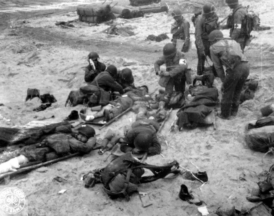 Médicos en combate del 4 del ejercito de los Estados Unidos, se ocupan de varias víctimas que yacen en camillas en la arena. Se cree que la foto fue tomada entre los días 6 al 7 de junio de 1944.