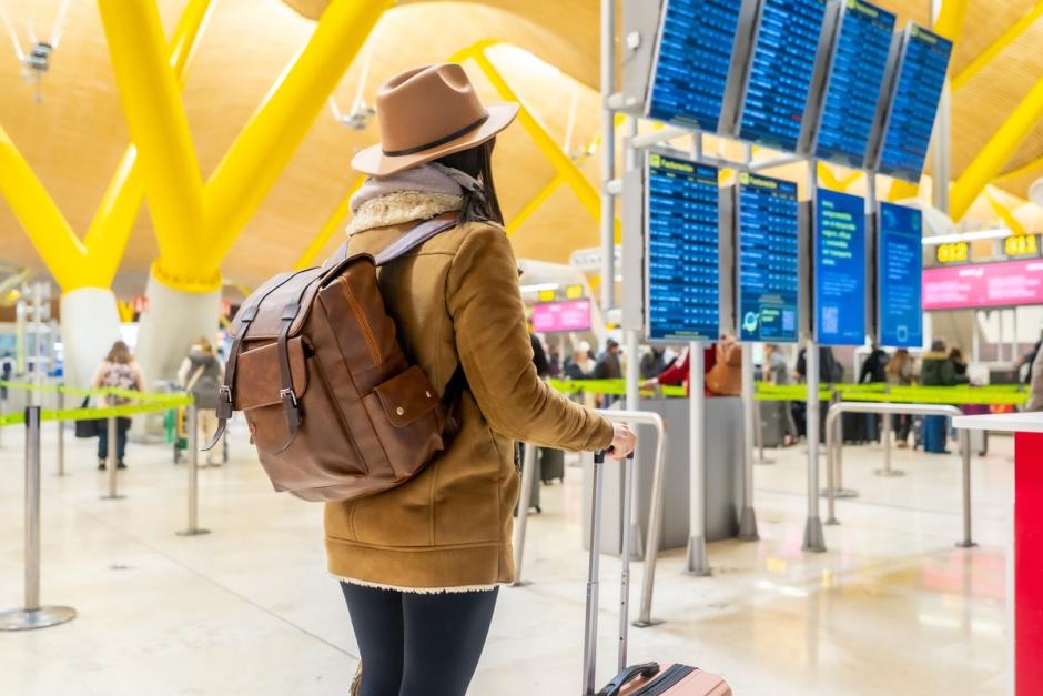 Viajera en el aeropuerto frente al panel de vuelos