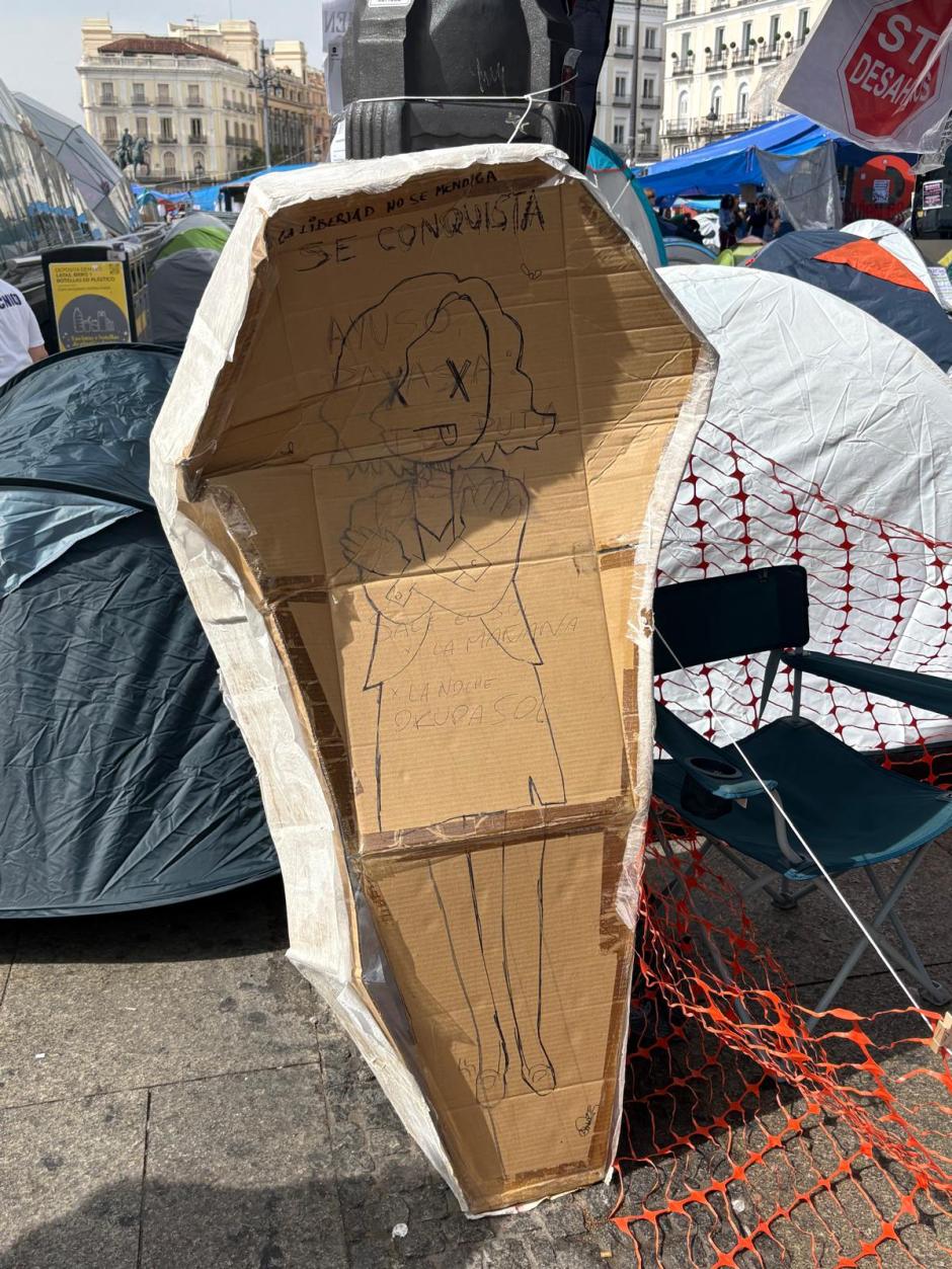 Ataúd de cartón con Isabel Díaz Ayuso dibujada dentro en la acampada de Sol por la vivienda
